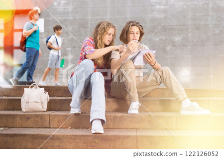 Girl prompts solution to problem to young man sitting on stone staircase in front of school Girl prompts solution to problem to young man sitting on stone staircase in front of school 122126052
