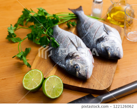 Two doradas on cutting board with herbs oil and lime 122126062