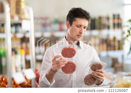 Man in light shirt choose and buy raw cooled semi-finished hamburger cutlet in store Man in light shirt choose and buy raw cooled semi-finished hamburger cutlet in store 122126087