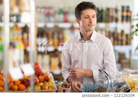 In store, man with purchases in hands looking for something on shelf of showcase 122126104