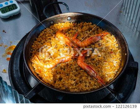 Process of cooking seafood paella in large frying pan 122126139