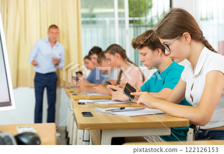 Teenager students sitting in class room with smartphones Teenager students sitting in class room with smartphones 122126153