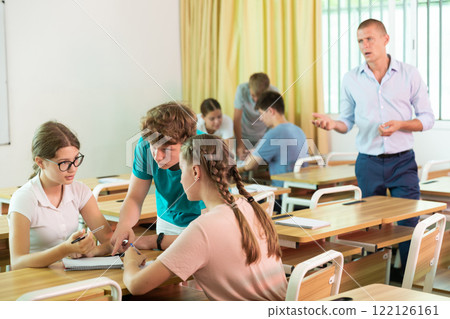 Teen girls and boys solving teacher assignments in small groups Teen girls and boys solving teacher assignments in small groups 122126161