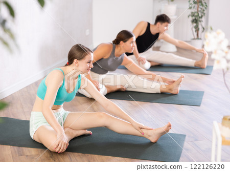 Young people doing one leg forward bend pose in class. Young people doing one leg forward bend pose in class. 122126220