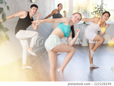 Sporty girl and guy practicing energetic dance moves with group in choreography class 122126244