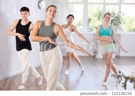 Group of happy sports girl and guy in activewear exercising dynamic dancing movemens in gym studio Group of happy sports girl and guy in activewear exercising dynamic dancing movemens in gym studio 122126258