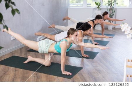 Girl performs bird dog pose, dandayamana hanumanasana, balancing table pose, group class 122126265