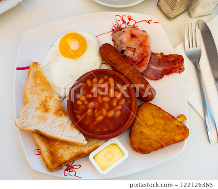 English breakfast of fried egg, bacon, sausage, toasts, stewed beans, hash brow 122126366