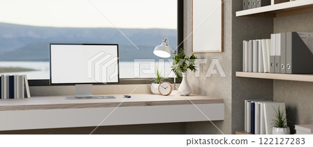 A computer with a white screen mockup and decor placed on a desk against a large window. 122127283