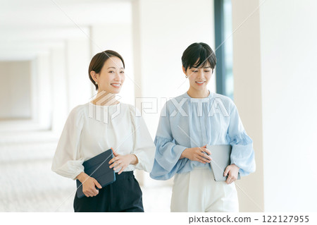 Two women walking down an office corridor 122127955