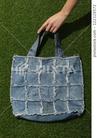 Handmade denim bag in hand on green background, top view 122128572