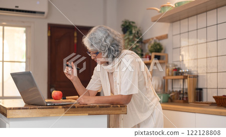 A positive, relaxed retired elderly Asian woman learns a new recipe from the internet in the kitchen 122128808