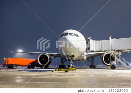 Front view of the white wide body passenger aircraft at the air bridge on night airport apron 122128963