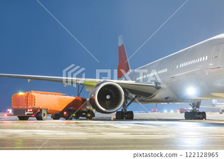 Airfield tanker refuels a wide-body passenger aircraft on the night airport apron 122128965
