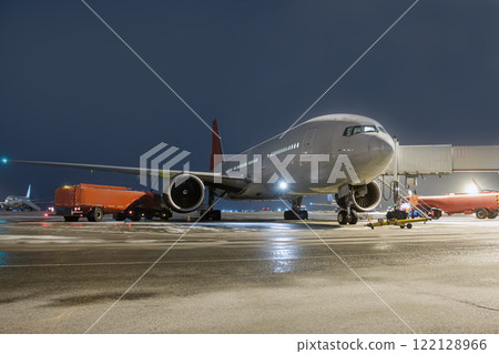 Wide body passenger airliner at the air bridge on night airport apron. Airfield tankers refuels aircraft 122128966