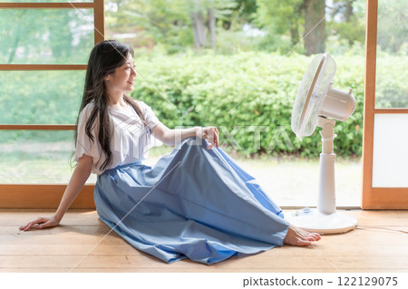 一位年輕女子在一棟古老民宅的門廊上在風扇前放鬆 122129075