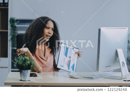 Female business person using digital tablet and laptop or remote working at home office, looking at digital tablet watching webinar, learning training, studying online seminar or video calling. 122129248