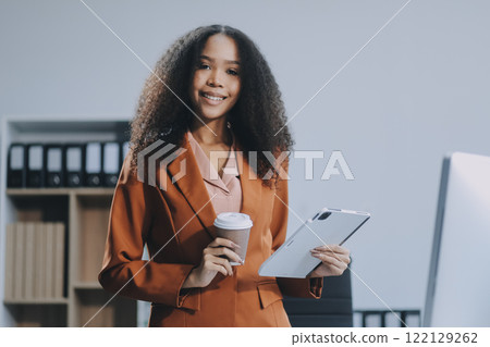 Beautiful young Asian businesswoman smiling holding a coffee mug and laptop working at the office. 122129262