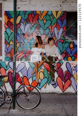 A couple poses by a colorful heart mural in the city, happily enjoying each other 122129570