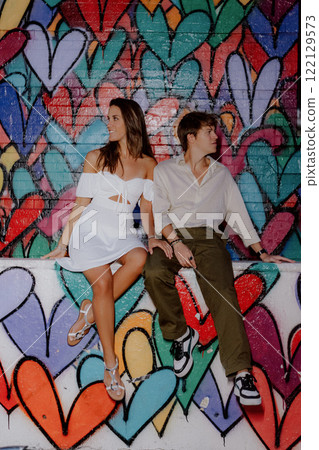 A couple poses by a colorful heart mural in the city, happily enjoying each other 122129573