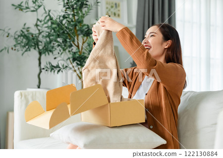 Happy young Asian woman opening delivery package at home 122130884