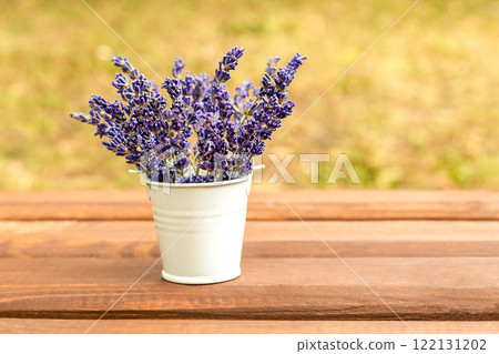 Purple lavender flowers collected in a white bucket on a wooden table. Place for an inscription. Selective focus. Purple lavender flowers collected in a white bucket on a wooden table. Place for an inscription. Selective focus. 122131202