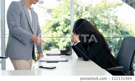 A serious, dissatisfied Asian male boss points at a document in front of a female employee. 122131564