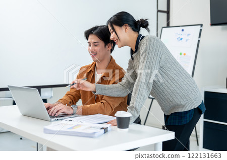 Two positive Asian businesspeople brainstorm and discuss a project together in a modern office. Two positive Asian businesspeople brainstorm and discuss a project together in a modern office. 122131663