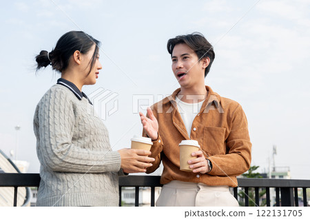 Two serious Asian employees engage in a conversation on the office rooftop during a coffee break. 122131705