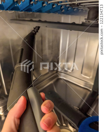 A close-up of a steam cleaner nozzle cleaning the inside of a dishwasher. High quality photo 122134713