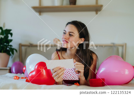 Beautiful woman lying on bed and reading love letter, gift card. Concept of Valentine's Day, love and romance. Beautiful woman lying on bed and reading love letter, gift card. Concept of Valentine's Day, love and romance. 122135324