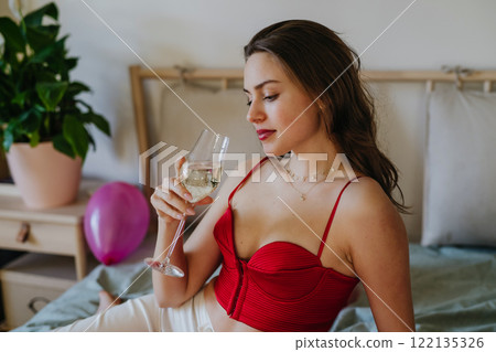 Radiant woman drinking champagne from a glass, dressed in a sexy red corset. Concept of Valentine's Day, love and relationship Radiant woman drinking champagne from a glass, dressed in a sexy red corset. Concept of Valentine's Day, love and relationship 122135326