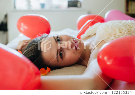 Sensual woman lying of bed in the middle of heart shaped baloons. Concept of Valentine's Day, love and relationship Sensual woman lying of bed in the middle of heart shaped baloons. Concept of Valentine's Day, love and relationship 122135334