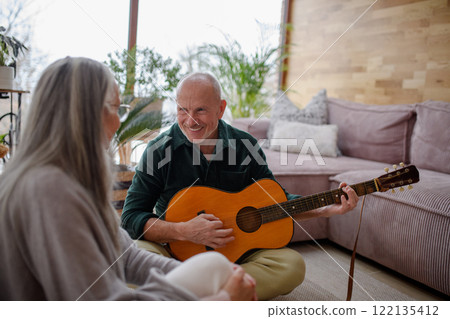 Real older couple at home. Husband playing music on a guitar for his wife. 122135412