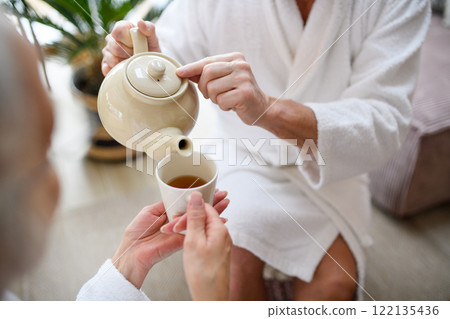 Close up of couple, after a spa session, sitting in relaxation room, drinking tea. Romantic wellness getaway. Close up of couple, after a spa session, sitting in relaxation room, drinking tea. Romantic wellness getaway. 122135436