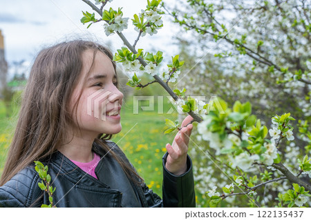 Teenage girl softly caressing blossoming tree limb, experiencing serene springtime garden moment Teenage girl softly caressing blossoming tree limb, experiencing serene springtime garden moment 122135437