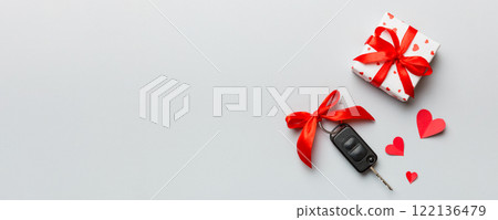 Black car key in a present box with a ribbon and red heart on colored background. Valentine day composition Top view 122136479