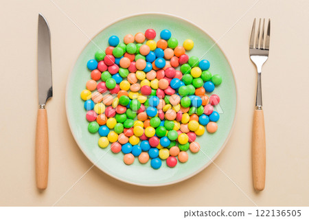 cutlery on table and sweet plate of candy. Health and obesity concept, top view on colored background 122136505