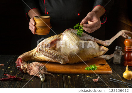 Hands skillfully season a fresh turkey with aromatic herbs and spices on a wooden cutting board. The warm atmosphere of a country kitchen adds to the culinary creativity Hands skillfully season a fresh turkey with aromatic herbs and spices on a wooden cutting board. The warm atmosphere of a country kitchen adds to the culinary creativity 122136612