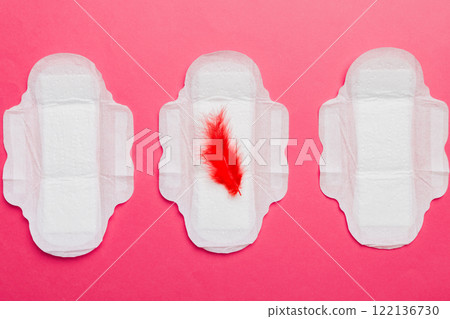 Women hygiene products or Sanitary pad with red feather on colored background. Pastel color. Closeup. Empty place for text. Female daily hygiene Women hygiene products or Sanitary pad with red feather on colored background. Pastel color. Closeup. Empty place for text. Female daily hygiene 122136730