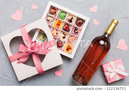 Bottle of red wine on colored background for Valentine Day with gift and chocolate. Heart shaped with gift box of chocolates top view with copy space Bottle of red wine on colored background for Valentine Day with gift and chocolate. Heart shaped with gift box of chocolates top view with copy space 122136751