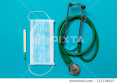 Top view of stethoscope, mercury thermometer and a protective face mask on colorful background. Medical equipment and health care concept Top view of stethoscope, mercury thermometer and a protective face mask on colorful background. Medical equipment and health care concept 122136815