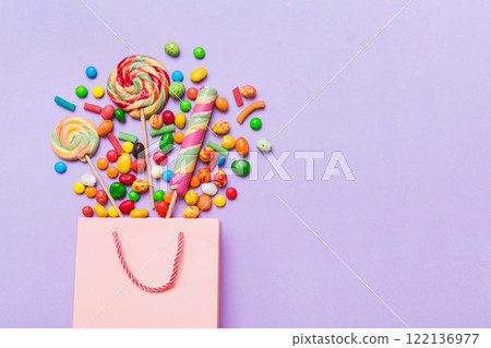 shopping paper gift bag in corner full of assorted traditional candies falling out on colored background with copy space. Happy Holidays sale concept shopping paper gift bag in corner full of assorted traditional candies falling out on colored background with copy space. Happy Holidays sale concept 122136977