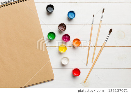 Album pages and paints, pencils, brush on a colored background. Top view with empty space. workplace for creativity. home teaching concept drawing 122137071