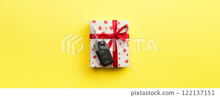 Car key on paper gift box with red ribbon bow and heart on yellow table background. Holidays present top view concept Car key on paper gift box with red ribbon bow and heart on yellow table background. Holidays present top view concept 122137151