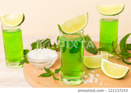 Sweet refreshing mint liqueur, with ice and mint leaves on table background, Shots with lime slice and mint flat lay Sweet refreshing mint liqueur, with ice and mint leaves on table background, Shots with lime slice and mint flat lay 122137243