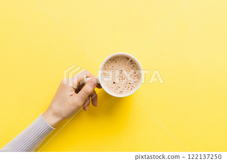 Minimalistic style woman hand holding a cup of coffee on Colored background. Flat lay, top view cappuccino cup. Empty place for text, copy space. Coffee addiction. Top view, flat lay 122137250