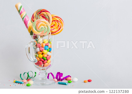 Colorful candies in cup on table on light background background. Large swirled lollipops. Creative concept of a jar full of delicious sweets from the candy store Colorful candies in cup on table on light background background. Large swirled lollipops. Creative concept of a jar full of delicious sweets from the candy store 122137280