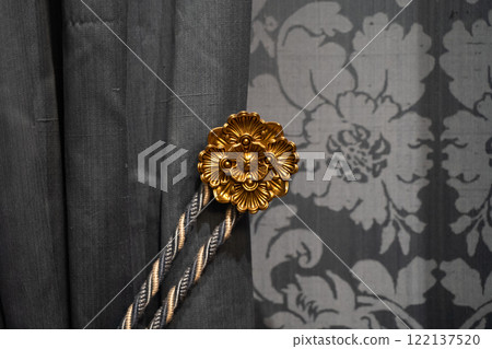 Ornamental gold tieback on grey curtain closeup 122137520