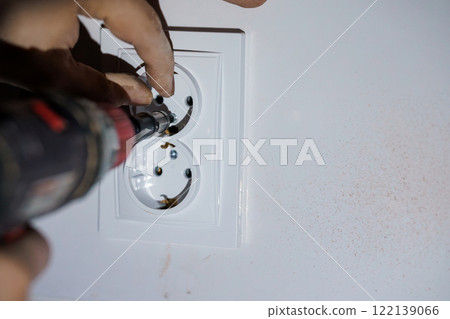 Close-Up of a Hand Installing a Dual Electrical Outlet with Power Drill Close-Up of a Hand Installing a Dual Electrical Outlet with Power Drill 122139066